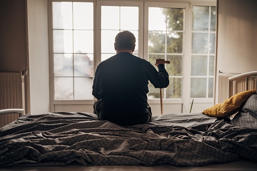 elderly man sitting on the edge of the bed with a cane