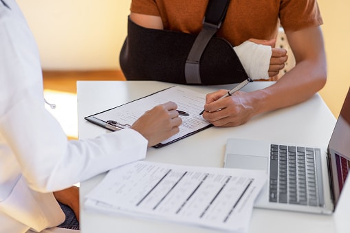 male in sling signing papers at medical facility